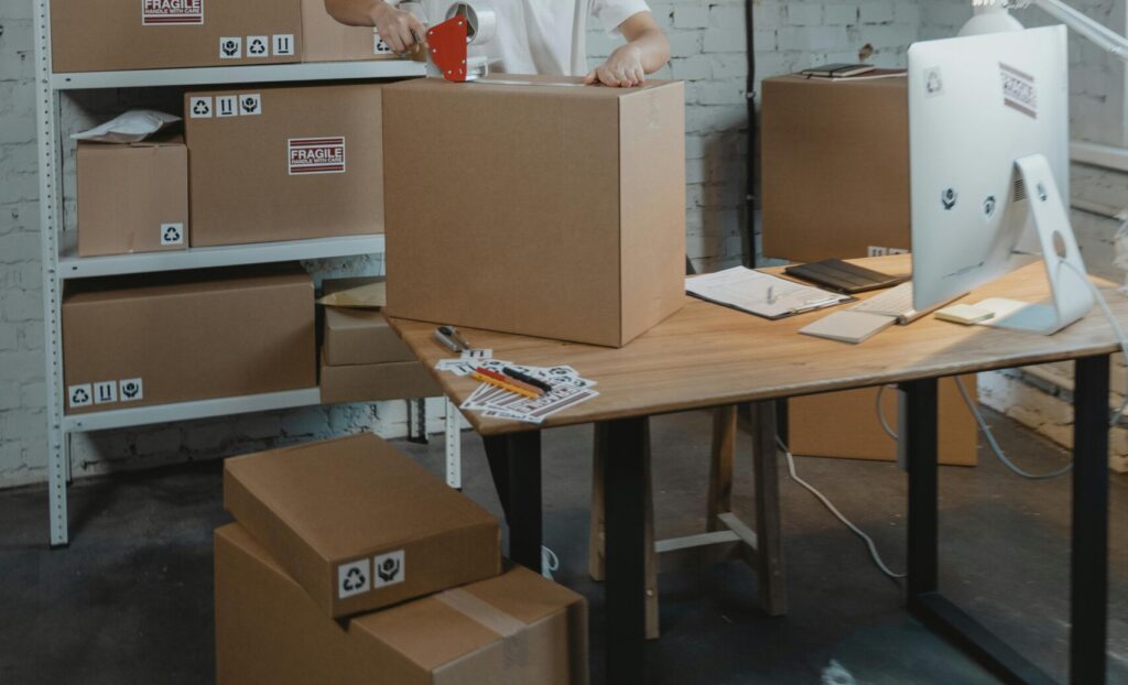 A warehouse worker in uniform packaging boxes for delivery in an organized storage area.