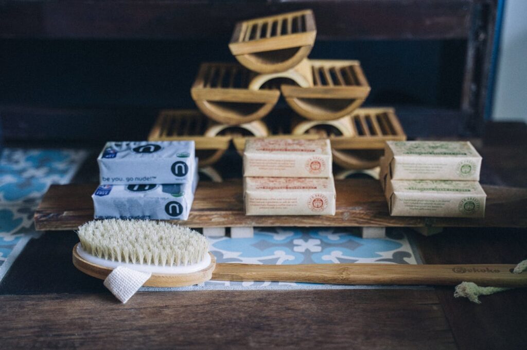 A close-up of a bamboo brush with handmade eco-friendly soap bars on a wooden shelf.